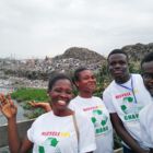Junge Menschen vor einem mit Müll verschmutzten Ufer